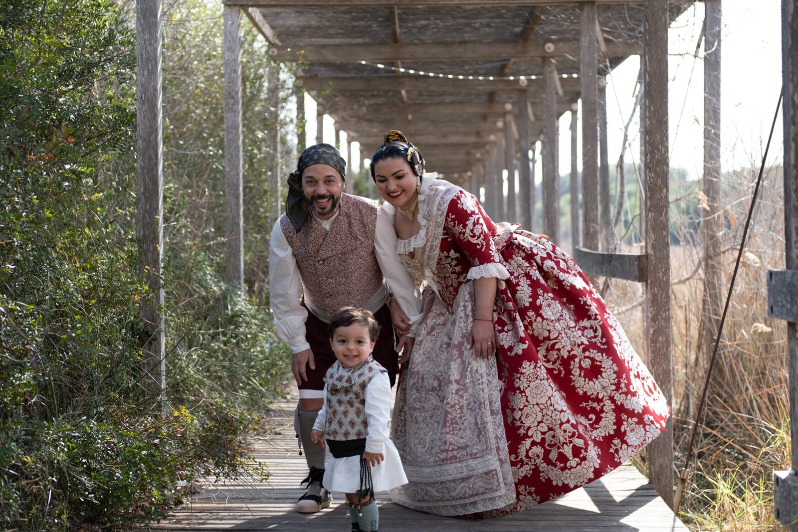 Familia con trajes tradicionales valencianos posando sonriente bajo una estructura de madera en un entorno natural.