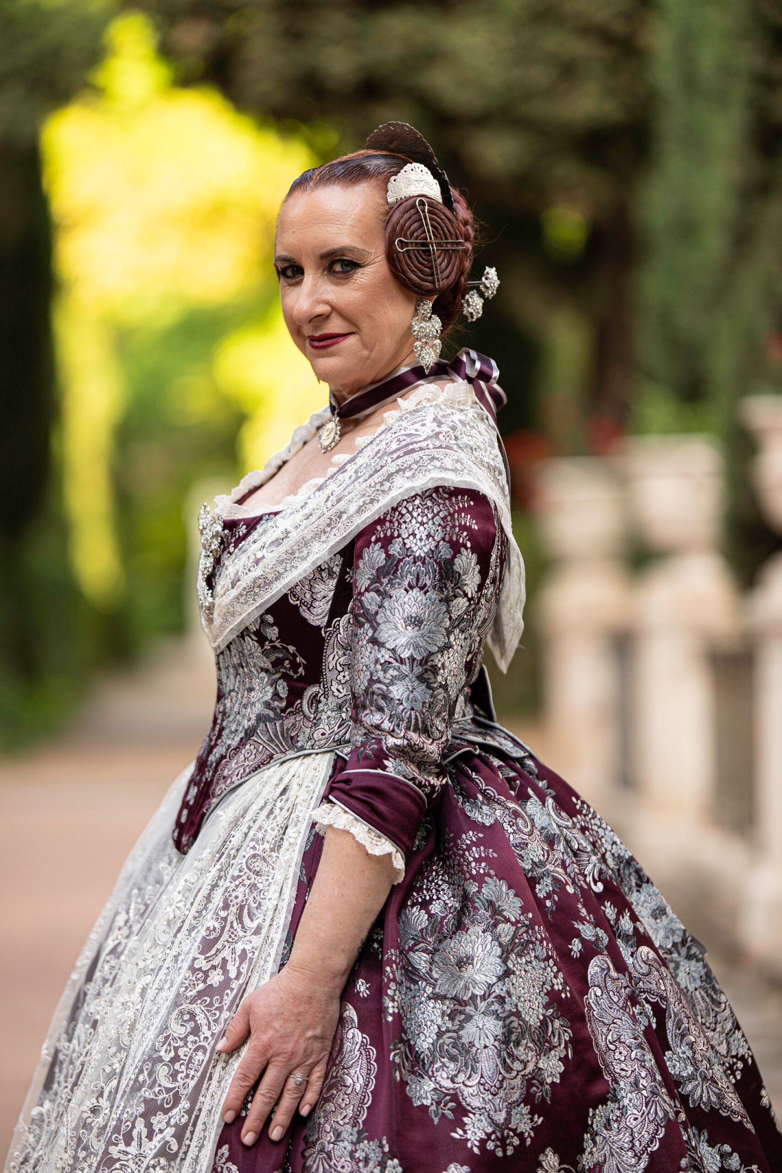 Fallera con traje clásico en jardín botánico o parque, reflejando la belleza y la artesanía del vestuario festivo de Valencia